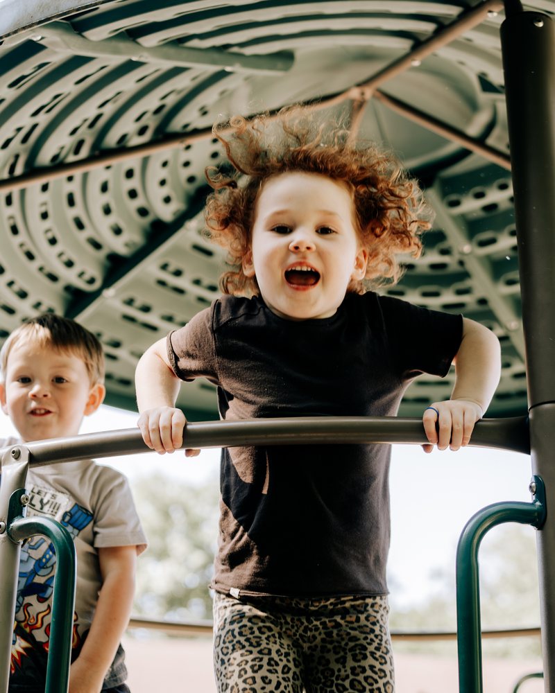 A girl cheering as she climbs the play structure