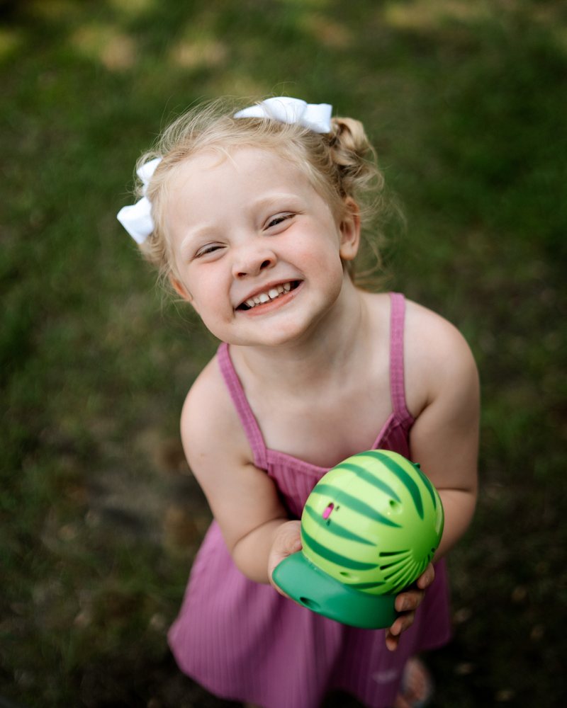 A girl holding a watermelon ball and smiling up at the camera