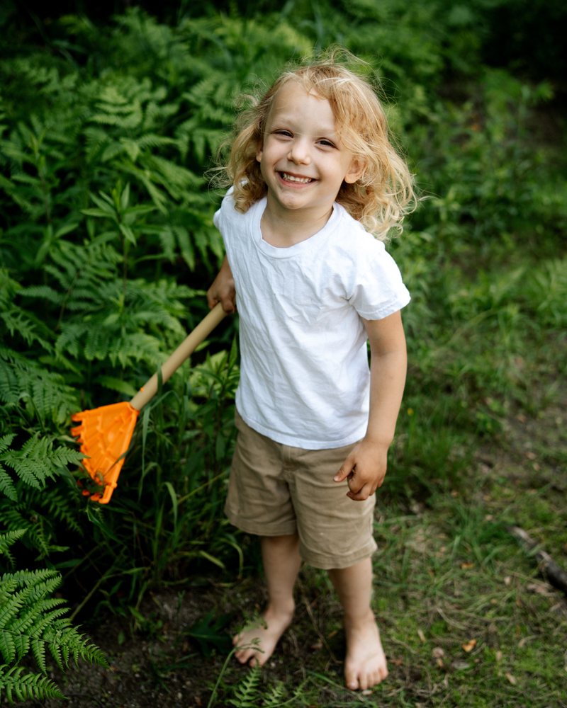 A barefoot child with a toy rake in the garden