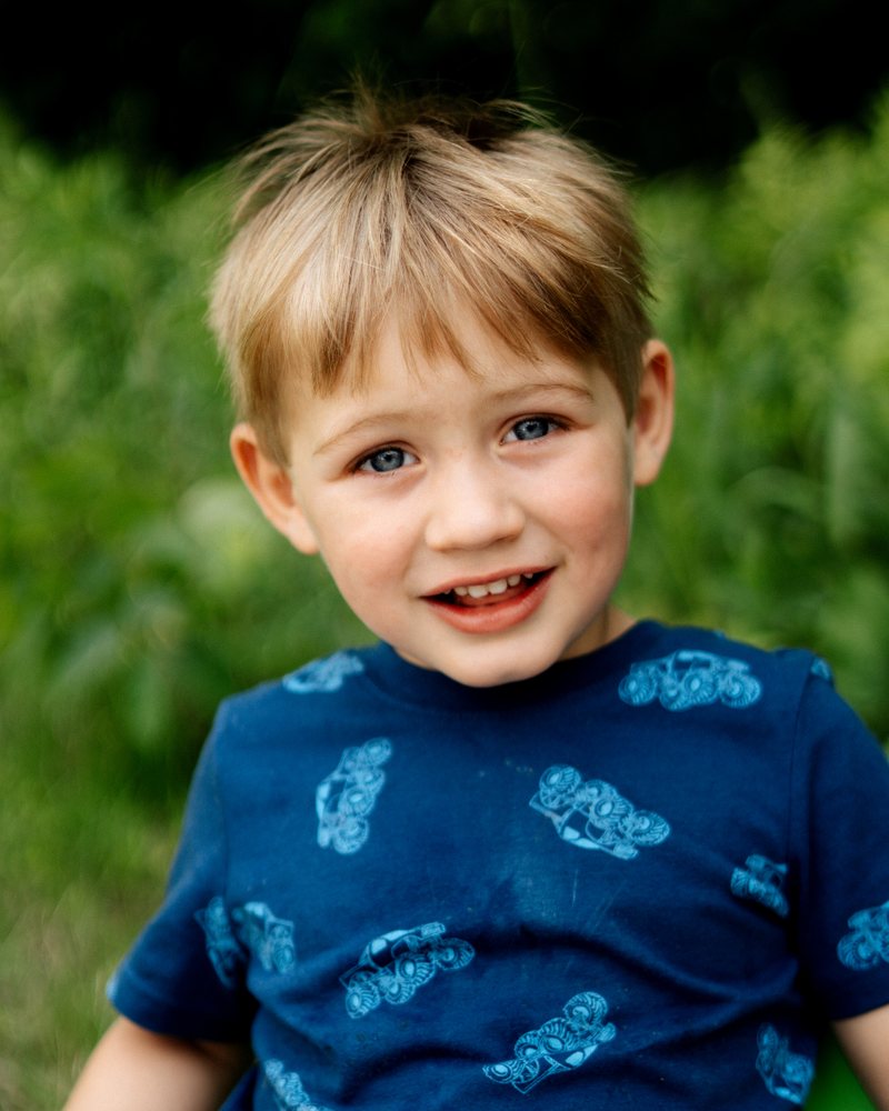 A boy in a blue shirt smiling outdoors
