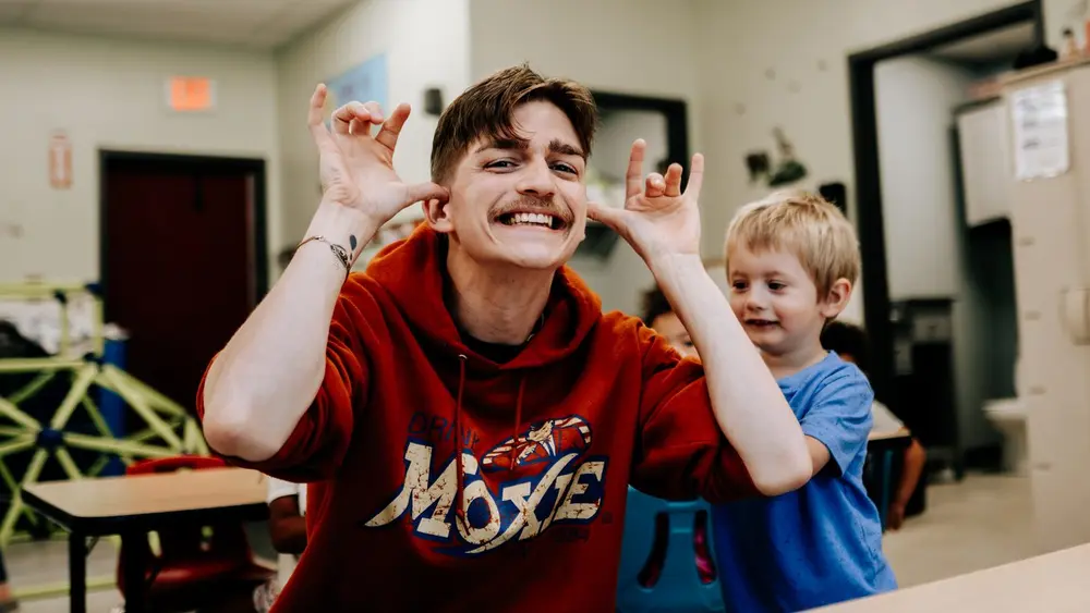 A Kids & Co. teacher pulling a silly face with a child in the classroom