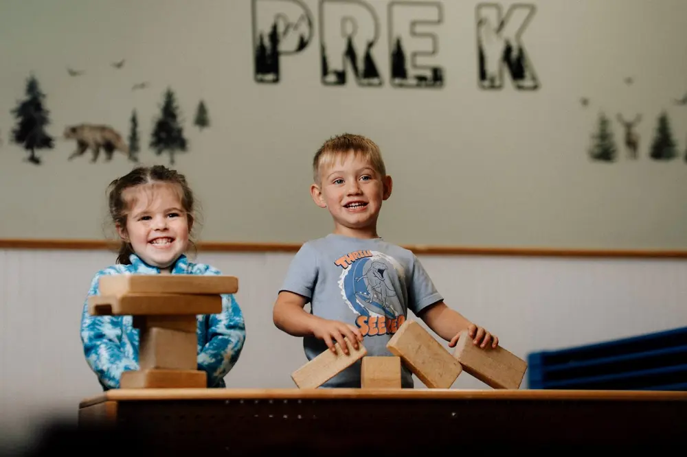 Two children building with wooden blocks under the Pre K sign
